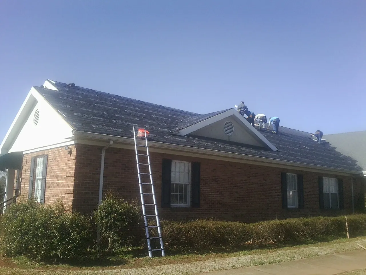 Crew tearing shingles off a brick ranch roof with a ladder set — Metal Roof Repair work by our crew in Carey