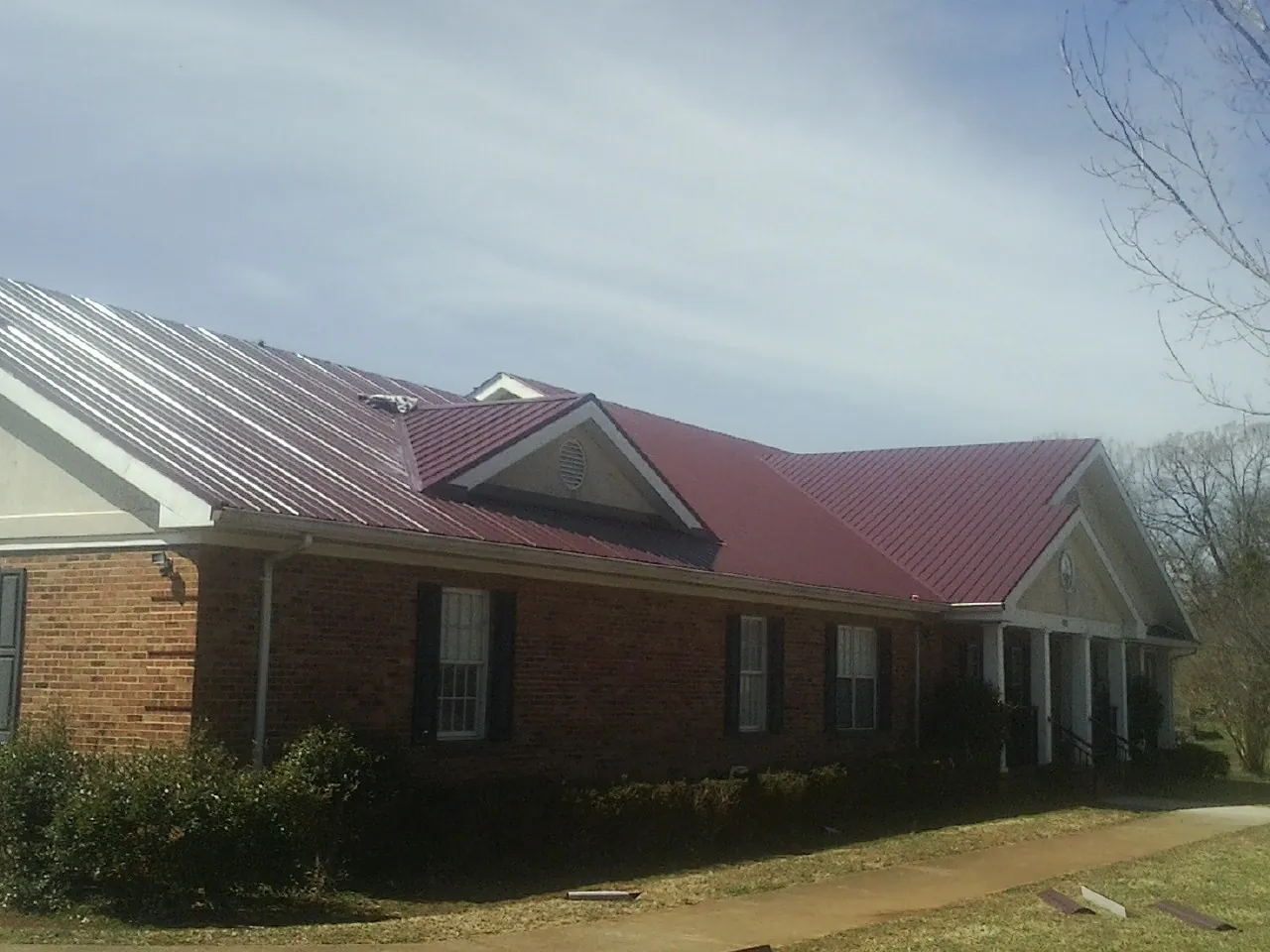 Red metal roof with gabled entries on a long brick building, from a Hail Damage Roof Repair job in Carey