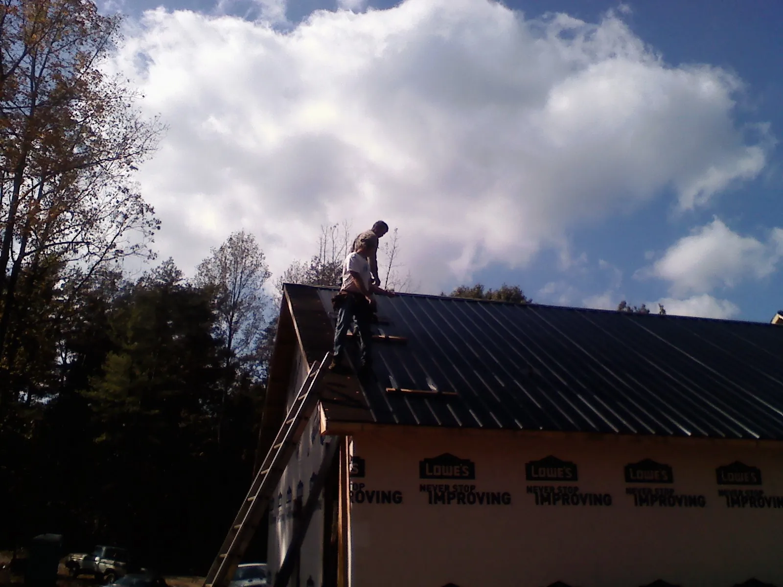Roofer fastening dark metal panels high against a cloudy sky, from a Roof Inspection job in Carey