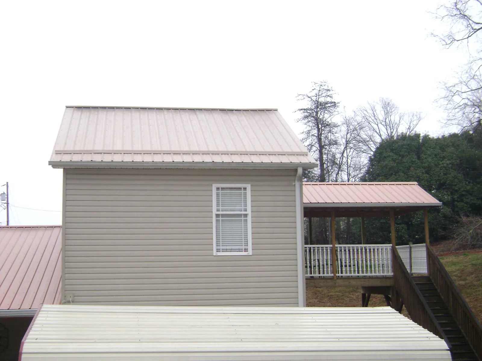 Tan metal roofs on a two story addition and attached porch, from a Roof Replacement job in Carey